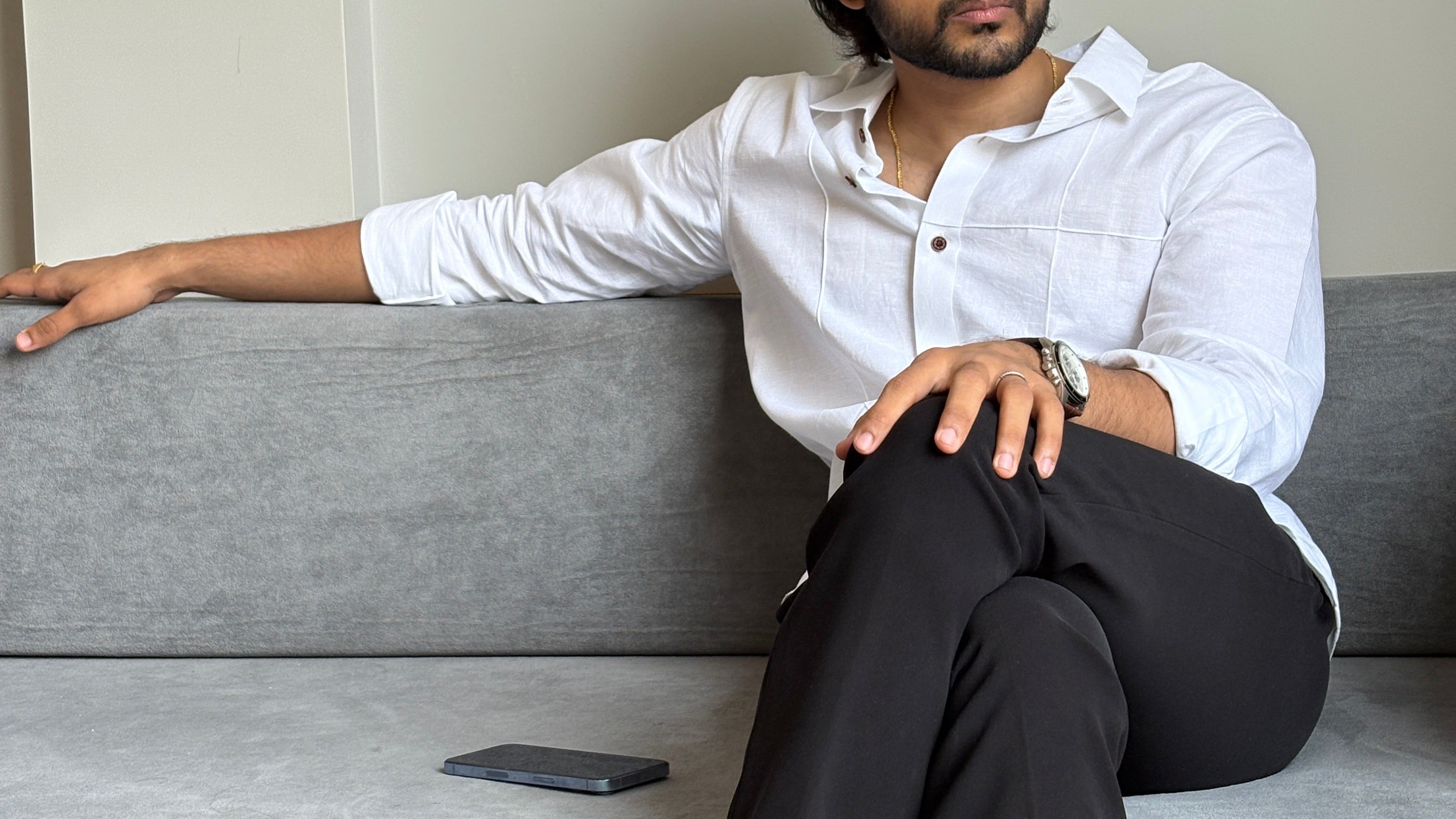 Person in cross white buno shirt and black pants leaning seated in a sofa.